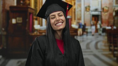 Mezuniyet şapkalı genç İspanyol kadın kilise ortamında neşeli bir şekilde gülümsüyor. Başarıyı ve sonsuz olasılıkların geleceğini simgeliyor..