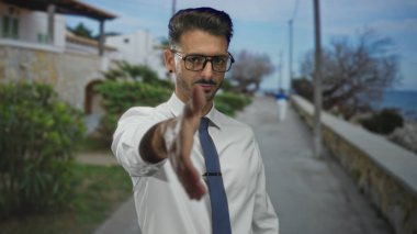 Beyaz gömlekli ve mavi kravatlı genç adam sokakta uzanmış el sıkışma teklif ediyor; dostça selamlaşma.