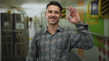 Yolcu teknesi koridorundaki genç adam neşeli bir gülümsemeyle iyi bir jest yapıyor, deniz yolculuğu sırasında rahatlama gösterisi yapıyor..