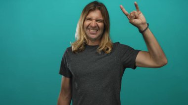 Sarışın, uzun saçlı, çıplak kollu sırıtan ve stüdyoda rock boynuzlarını gösteren bir adam..