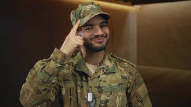 Kamuflaj üniforması giyen genç bir İspanyol ve künyesi stüdyoda parmak uçlarına dolaşmış..