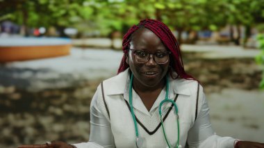 Açık hava parkında steteskopla gülen kadın, bulanık doğal bir arka plana karşı neşeli yüz ifadesini sergiliyor..