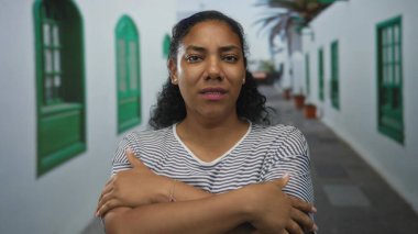 Beyaz duvarlar ve yeşil pencere panjurları ile çevrili dar eski kasaba caddesinde dururken avuçlarını ovuşturan Afrikalı Amerikalı kadın..