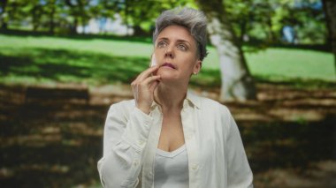 Kısa saçlı, beyaz gömlekli bir kadın, hafif kaşları çatık ve gözleri kapalı olarak el ele tutuşuyor..