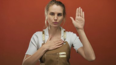 Göğüs göğüse söz veren, önlük giyen, canlı kırmızı arka plana karşı duran, samimiyet ve bağlılığı somutlaştıran, dürüstlük ve adanmışlık teması için mükemmel bir kadın..