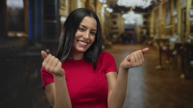 İspanyol kadın, elleri ile bir işaret hareketi yapıyor kapalı, zarif kilise dekoru ile çevrili, kırmızı bir gömlek giyiyor ve dostça bir davet yayıyor.