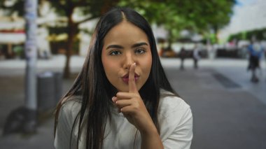 Kalabalık bir caddede sessiz sessiz hareketler yapan İspanyol kadın şehir ortamında ağaçlar ve insanlar tarafından çevrelenmiş durumda.