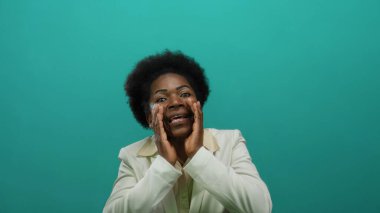 İzole edilmiş yeşil arka plana karşı tutkuyla bağıran bir kadın beyaz takım elbise giyiyor, elleri ağızda ifade ediyor, iletişim kuruyor, duygu kuruyor..