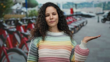 Kıvırcık saçlı genç İspanyol kadın, şehir sokağının önünde sıra sıra bisikletlerle el ele tutuşarak açık havada dostane ve misafirperver bir ortam yaratıyor..