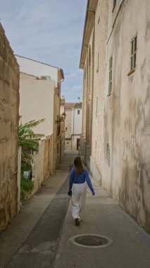 Mallorca 'nın eski kasabasında, açık gökyüzünün altında geleneksel Akdeniz mimarisini sergileyen bir kadın dar bir sokakta yürüyor..