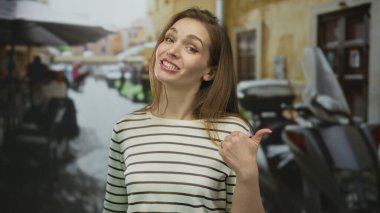 Beyaz kadın gündüz vakti kalabalık şehir caddesinde gülümseyip başparmağıyla işaret ediyor..