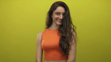 İspanyol kadın turuncu bluz giyiyor, çıplak omuzlarını gösteriyor ve stüdyoda başını eğerken gülümsüyor; mutluluk..