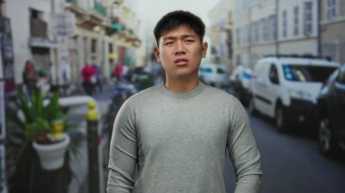 Sokaktaki genç adam, arka planda trafik ve yayaların görüldüğü hareketli bir şehir sahnesinde kargaşa yaratıyor.