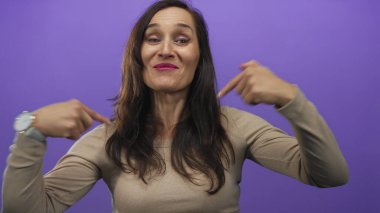 İspanyol kadın gülümsüyor ve kendini izole edilmiş mor bir arka plan üzerinden gösteriyor. Stüdyo ortamında kendine güven ve pozitifliği somutlaştırıyor..