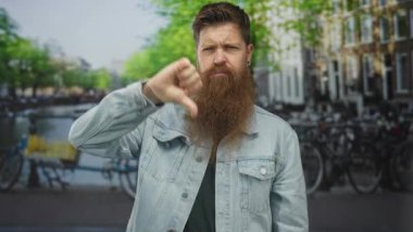 Uzun sakallı bir adam açık havada bir kanalda işlek bir caddede açık bir baş parmak hareketi yapıyor. Hayal kırıklığı..