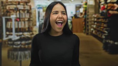 Raflarla çevrili bir mağazada neşeli bir şekilde gülümseyen kadın, moda ve perakendeciliği ön plana çıkaran kapalı bir alışveriş deneyimini yakalıyor..