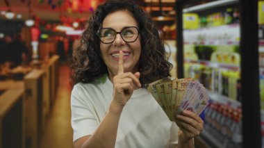 Meksika pezosu tutan bir kadın canlı bir restoran ortamında sessizlik için jestler yapıyor. Gizlilik, finans ve kültürü somutlaştıran bir mizah anlayışı var. İlginç bir iç mekan sahnesi yaratıyor..