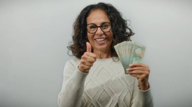 Elinde Dirham banknotlarıyla gülümseyen bir kadın beyaz arka planda başparmak işareti yaparak finansal başarı ya da tatmin öneriyor..