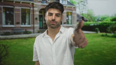 Beyaz tişörtlü, bina girişinde baş parmak hareketi yapan İspanyol bir genç. Onaylandı..