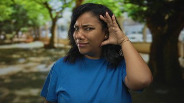 Afro-Amerikan kadın kulakları güneş ışığında yeşil şehir parkında yumuşak bulanık ağaçlarla; kafa karışıklığı.