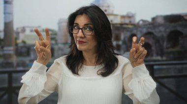 Gözlük takan kadın, antik sütunlara tepeden bakan Roma harabelerinde tırnak işareti yapıyor; şüphecilik.