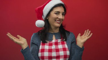 Noel Baba şapkası takan ve kırmızı önlük takan bir kadın stüdyoda açık avuçlar, bayram kutlamaları neşesini gösteriyor..