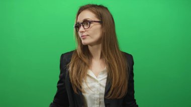 Kadın yeşil stüdyoda başını eğerek ve hafif bir gülümseme ile gözlerini kapayarak omuz silker; belirsizlik belirsizlik belirsizlik kafa karışıklığı.