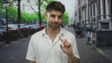 Genç adam park halindeki arabaların, tuğla bina cephelerinin ve ağaçların kuşattığı dar bir sokakta parmak göğse işaret ediyor..