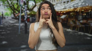 Çıplak omuzlu, uzun saçlı, gülümseyen ve parmaklarını sokakta yanaklara gösteren bir kadın..