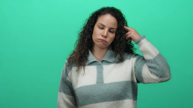 Kıvırcık saçlı İspanyol kadın, izole edilmiş stüdyo ortamında hayal kırıklığını ve hoşnutsuzluğunu ifade eden sert yeşil bir duvara doğru parmaklarıyla ateş ediyor..