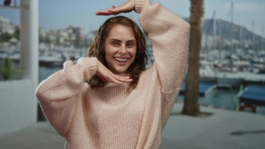 Sahil marinasında rahat bir kazakla gülümseyen bir kadın kayıklar ve palmiye ağaçları ile açık havada açık havada, açık bir gökyüzünün altında huzurlu bir anı yakalıyor..