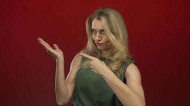 Gülümseyen ve avucuna işaret eden genç bir kadın canlı kırmızı bir arka plan, pozitiflik ve güven ifade ediyor.