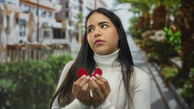 Kırık kalp sembolü taşıyan kadın, hüzün ve kalp kırıklığını resmediyor, canlı şehir manzarasıyla harmanlanıyor, resmedilmeye değer arka planda duygusal bir zıtlık olarak..