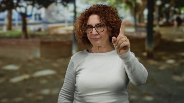 Kadın parkta, açık arka planda esmer kıvırcık saçlı gözlük takarak güneşli bir günde düşünceli bir anı işaret ediyor..