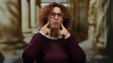 Kıvırcık saçlı, gülümseyen ve üniversite ortamında el kol hareketi yapan bir kadın akademik ortamda neşe saçıyor..