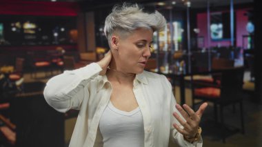 Kısa gri saçlı kadın binadaki sıcak tepe ışıkları altında ter parlatıcı ile el ele tutuşuyor..