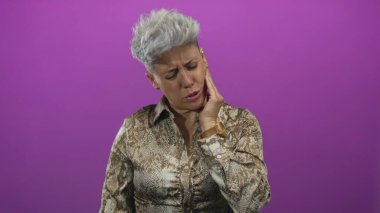 Mor bir stüdyo ortamında yanak tutan ve irkilen bir kadın desenli bluz giyiyor; diş ağrısı.