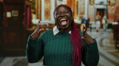 Kilisede canlı saçları ve yeşil süveteri olan bir kadın, bulanık mimari arka planda neşe ve duyguyu yakalıyor..