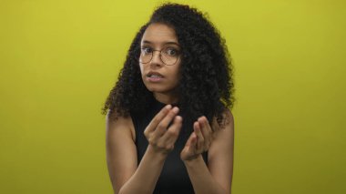 Genç İspanyol kadın, sarı bir duvarın üzerinden stüdyoda parmaklarını ovuşturarak endişeli bir bakış atar; çaresizce yardım için yalvarır..