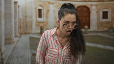 Kadın, eski bir bina avlusunda kendinden ötesine bakarken gözlerini kısar ve bardakları ayarlar..