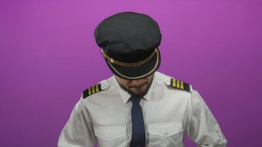 Pilot üniformalı genç İspanyol adam pembe arka plana bakıyor.