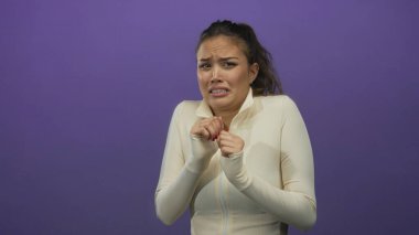 Beyaz elbiseli kadın, canlı mor bir arkaplan karşısında korkusunu dile getiriyor, soyutlanmış, duygusal ve gergin bir an sergiliyor..