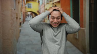 Renkli şehir caddesinde gülümseyen genç adam neşeli bir ifadeyle, günlük kıyafetler giyerek, gün içinde şehir ortamında mutluluk ve pozitiflik sergiliyor..