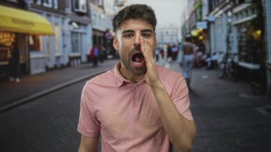 Pembe polo giyen, ağzı elle kaplayan genç İspanyol adam; yorgunluk, yorgunluk, bıkkınlık....