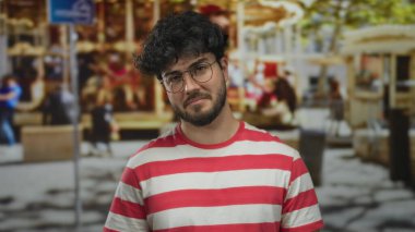 Sokak ortamında gözlüklü ve sakallı, kırmızı beyaz çizgili gömlek giyen üzgün, şehir geçmişi bulanık genç bir İspanyol..