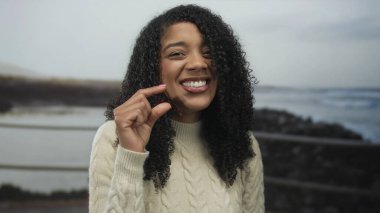 Kadın bulutlu bir gökyüzü altında deniz kenarında küçük bir gezinti için parmaklarını çimdikliyor; neşe küçücüğü.