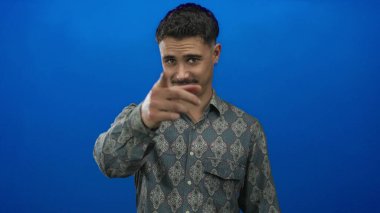 Genç adam kendine güvenen bir tişörtle izole edilmiş mavi bir arkaplanı işaret ederek dikkatleri üzerine çekiyor ve nişan alıyor..