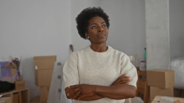 Kadın, yeni bir salonda kollarını kavuşturarak duruyor. Kutuları taşıyor ve gülümsüyor. Başarı ve yeni bir başlangıç hissi yakalıyor..