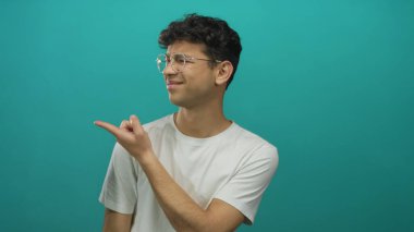 Gözlüklü beyaz gömlekli bir adam, tepe rengi stüdyo ortamında görülmemiş bir konuyu işaret ediyor..