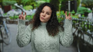 Canlı bir şehir ortamında kıvırcık saçlı kazak giyen bir kadın sokakta dikiliyor..